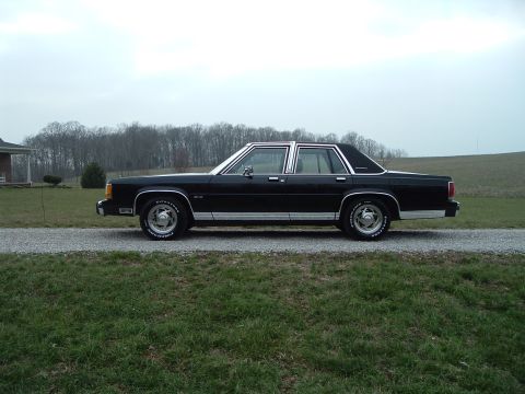 1989 Ford Crown Victoria LTD - A black sedan with chrome accents sits on a gravel road, with a house and trees in the background.