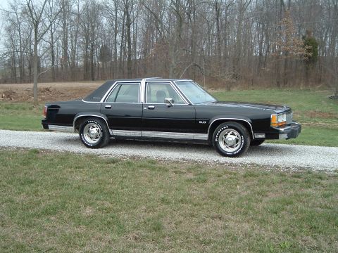1989 Ford Crown Victoria LTD - This black sedan is parked on a gravel driveway with a wooded area behind it.