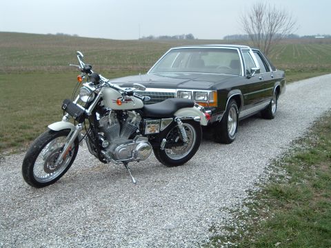 1989 Ford Crown Victoria LTD - A black 1989 Ford Crown Victoria LTD is parked on a gravel road next to a white motorcycle.