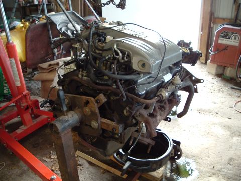 1989 Ford Crown Victoria LTD - Engine assembly being worked on, suspended by an engine hoist in a garage setting.