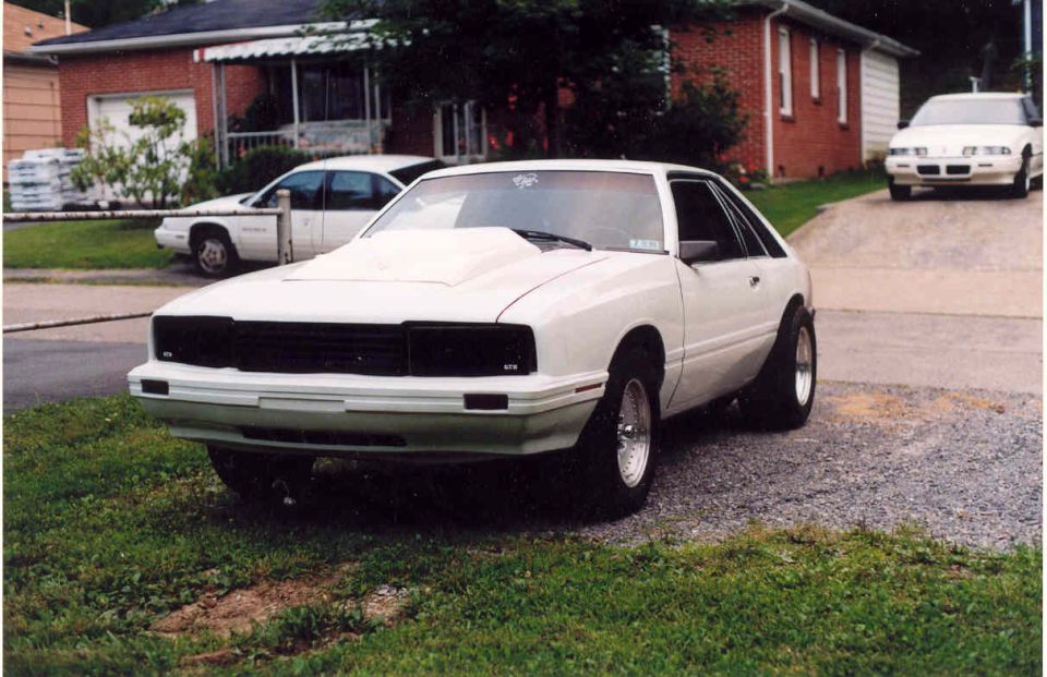 White Fox-body Mercury Capri drag car with cowl hood and roll cage, front 3/4 view