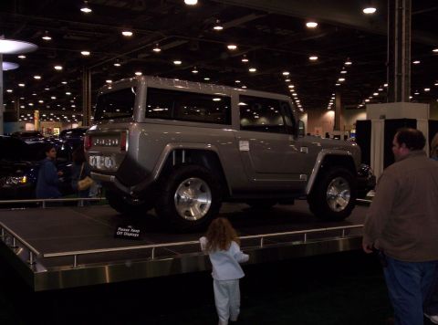 1989 Ford Bronco - A concept SUV is displayed on a platform at an auto show, with people observing.