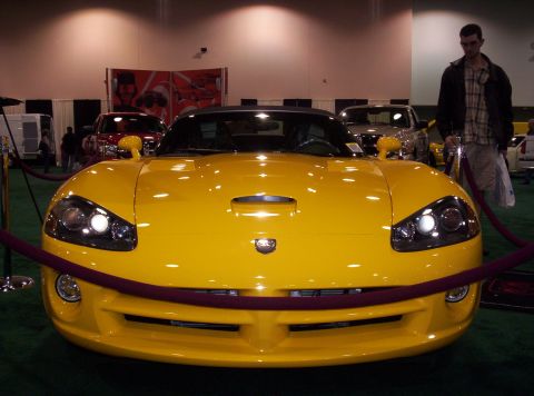 1989 Ford Bronco - A yellow sports car is displayed at an auto show with other vehicles in the background.