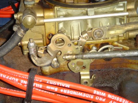 1975 Ford Ranchero - Close-up of a carburetor linkage system, with bright orange Mallory 8mm Sidewinder spark plug wires visible in the foreground.