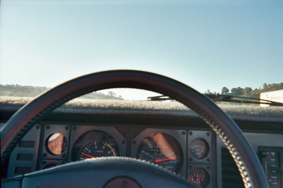 Driver's view over a leather-wrapped steering wheel and gauge cluster toward hilly terrain