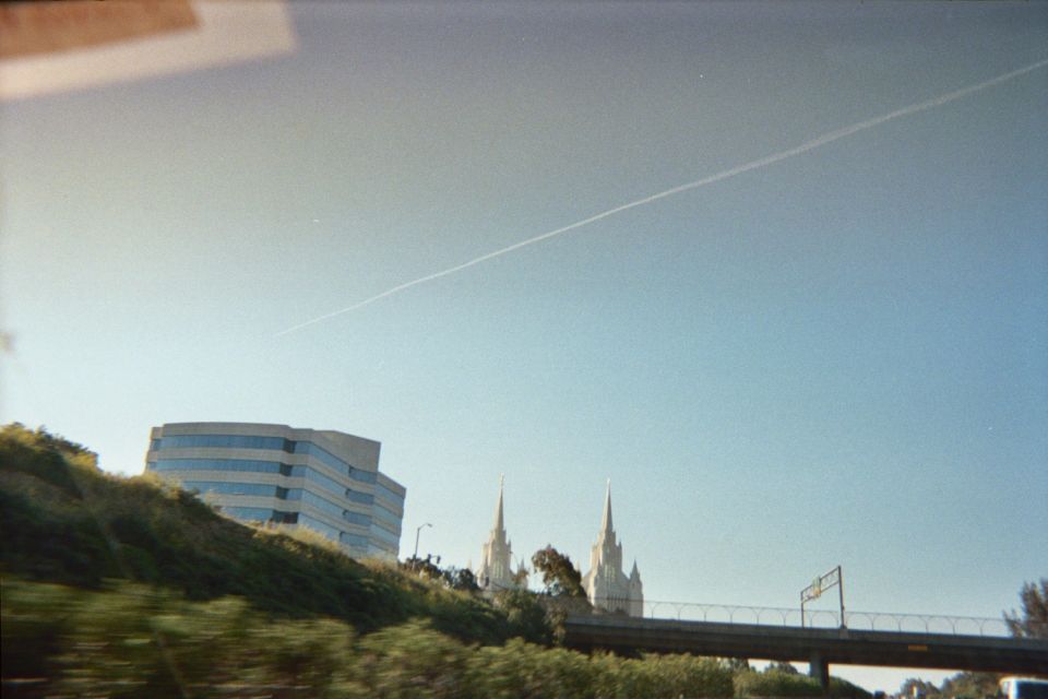 Twin-spired white temple and curved office building beside a freeway under a contrail sky