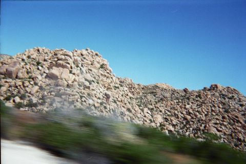 1990 Ford Bronco - rugged hillside of piled tan boulders and low green scrub rises against a deep blue sky.