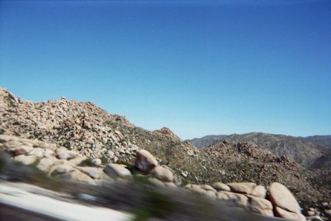 1990 Ford Bronco - Tan boulder ridges and distant blue mountains stretch beneath a clear sky in a blurred motion shot.