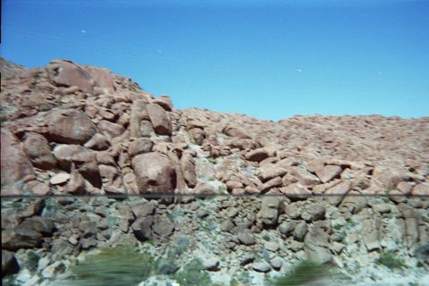 1990 Ford Bronco - steep embankment of reddish desert boulders and loose rock fills the frame below a clear blue sky.