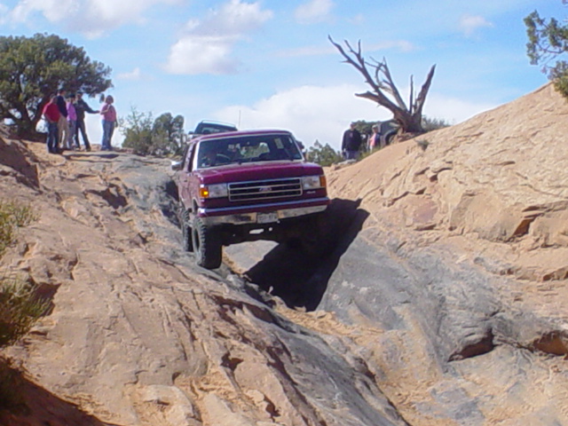 Purple lifted Ford truck crawling down a slickrock ledge on a desert trail