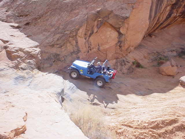 Blue open-top Jeep climbing slickrock in a red desert canyon