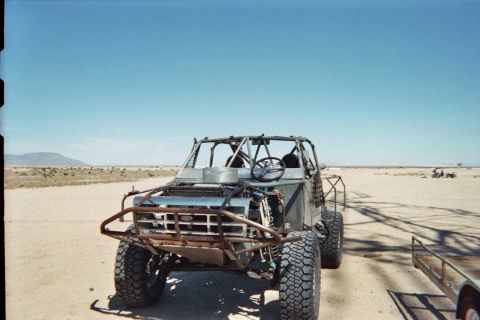 1990 Ford Bronco - bare tube-frame off-road race buggy with a brush guard and large knobby tires sits on open desert ground.