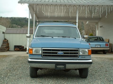 1990 Ford Bronco - Front view of a blue 1990 Ford Bronco parked in a driveway with another vehicle behind it.