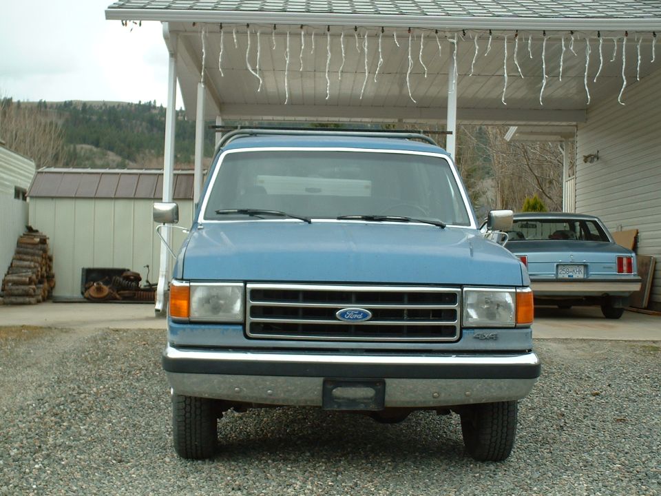 1990 Ford Bronco front view, parked under carport. Another car is visible in the background