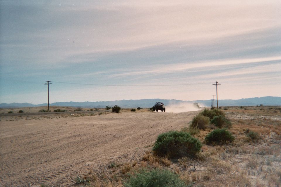 Dark vehicle raising dust on a graded dirt road lined with power poles in the desert