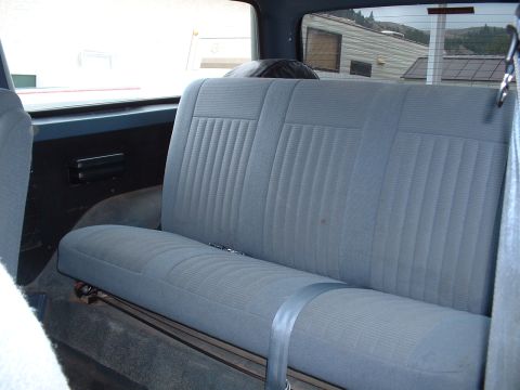 1990 Ford Bronco - The rear interior of a vehicle, showing the blue fabric seat and seatbelt, with a view out the back window.