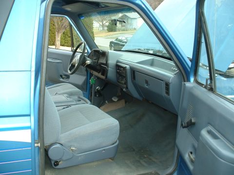1990 Ford Bronco - Interior view of a blue SUV, showing the dashboard, seats, and steering wheel with the hood open.