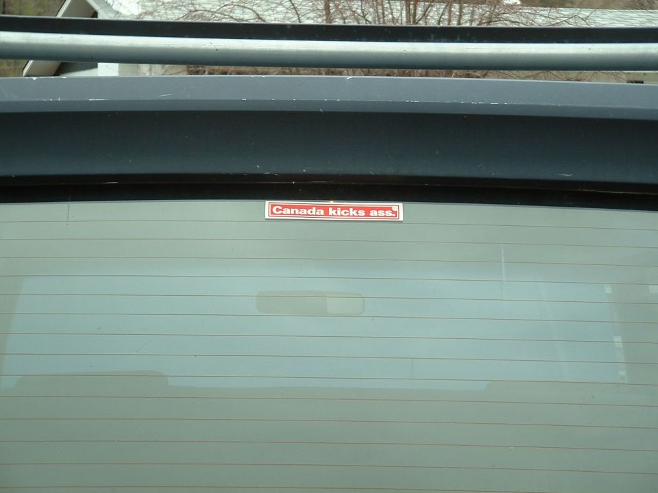Rear window of a vehicle with a "Canada kicks ass" sticker and a "SUPERMOTORS.net" watermark