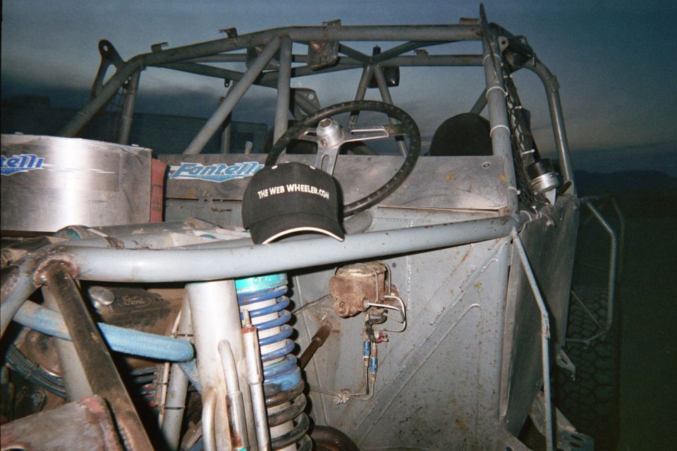 Engine and cockpit of a tube-frame buggy at dusk with a black cap reading TheWebWheeler.com