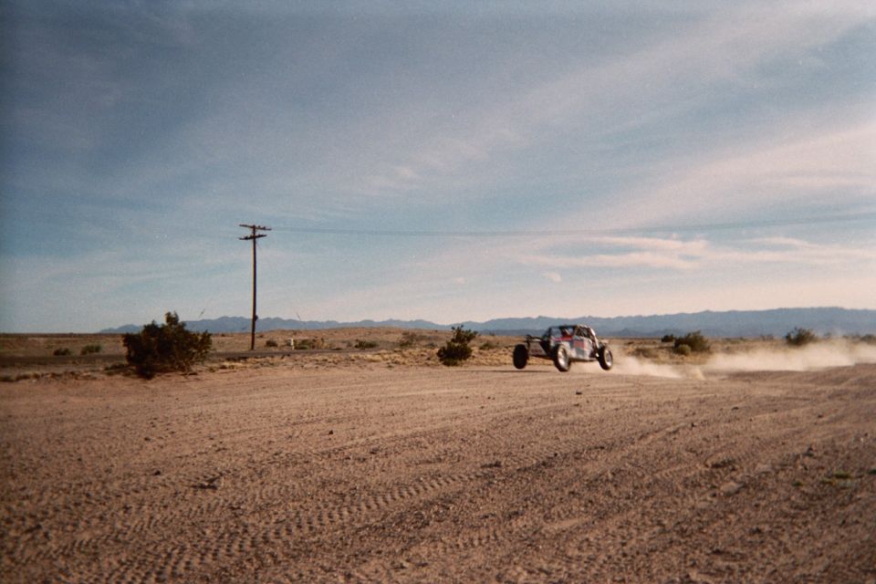 Off-road buggy speeding down a dirt road throwing dust, with mountains and a power pole