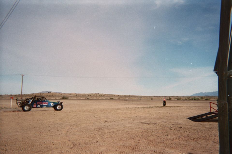 Blue open-frame sand rail parked on flat desert sand near a wind sock
