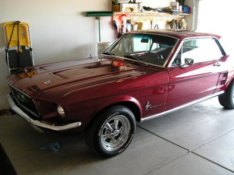 1967 Ford Mustang - Dark red 1967 Ford Mustang coupe parked in a garage with shelves and tools in the background.