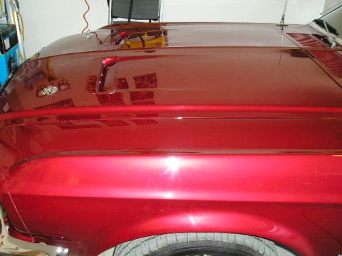 1967 Ford Mustang - Close-up of a shiny red car's hood and fender, showing reflections and a portion of the tire.