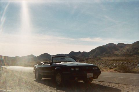 1985 Ford Mustang - A black 1985 Ford Mustang convertible sits parked on the shoulder of a road in a desert landscape.