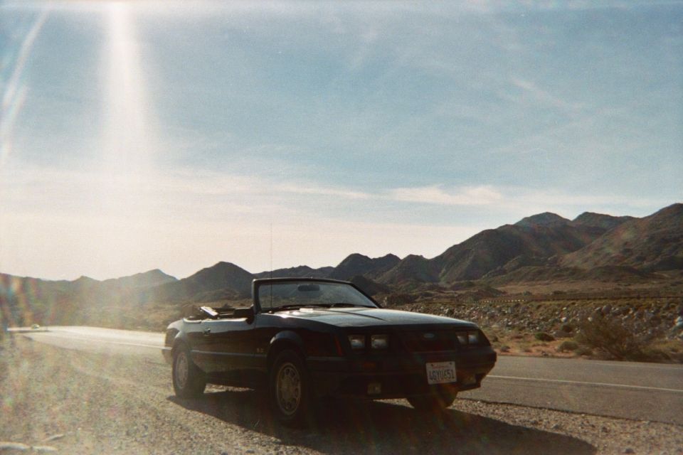 Black 1985 Ford Mustang convertible parked on side of desert road with mountains in background
