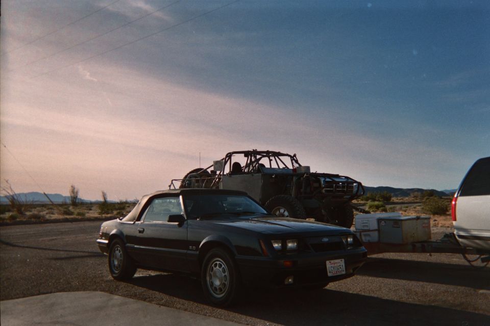Black 1985 Ford Mustang convertible parked next to a dune buggy in a desert landscape