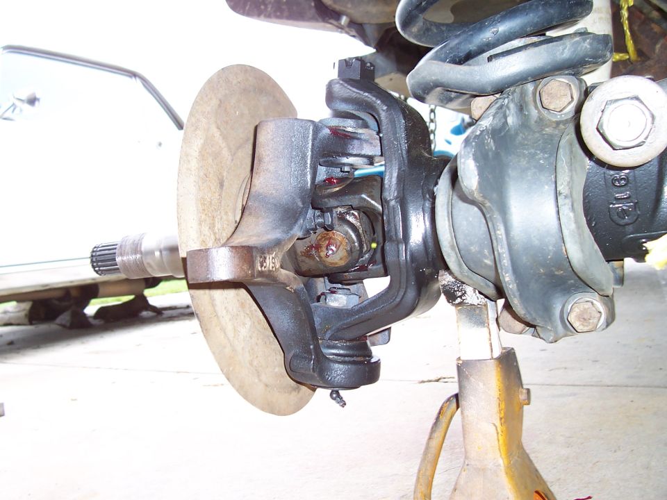 Close-up of a vehicle's front axle and suspension assembly, including a brake rotor and CV joint