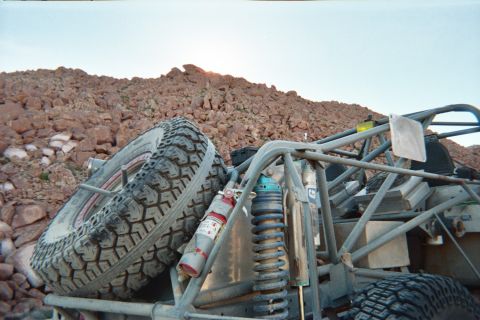 1990 Ford Bronco - Close view of a tube-frame off-road buggy showing its spare tire, coilover shocks and fire extinguisher against a rocky slope at dusk.
