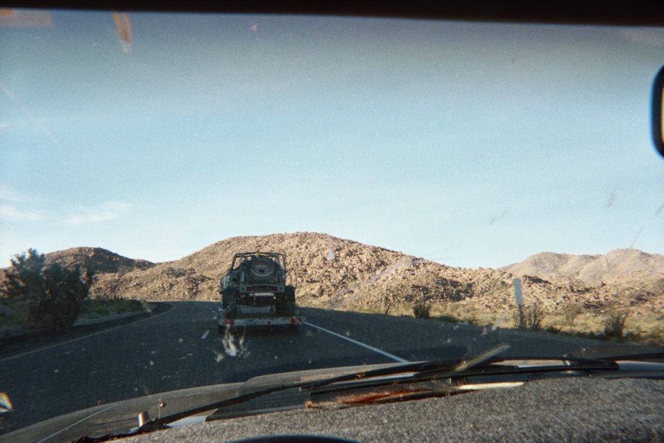 Windshield view of a Jeep-like vehicle towed on a trailer down a desert road