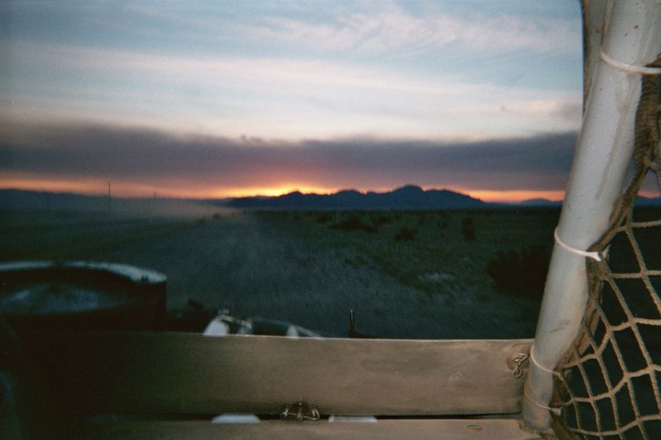 Sunset over distant mountains seen past a netted tube-frame vehicle window
