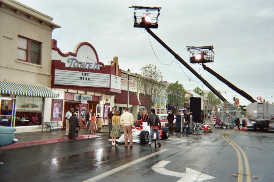Film crew with crane lights filming an open-wheel car on a main street