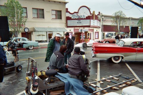 1990 Ford Bronco - film crew works around a camera dolly on a wet street lined with 1950s cars including a red convertible, near the Tower theater.