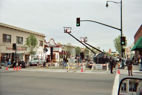 1990 Ford Bronco - Two camera cranes extend over a closed downtown intersection marked with Road Closed signs as crew and vintage cars stage near old storefro…