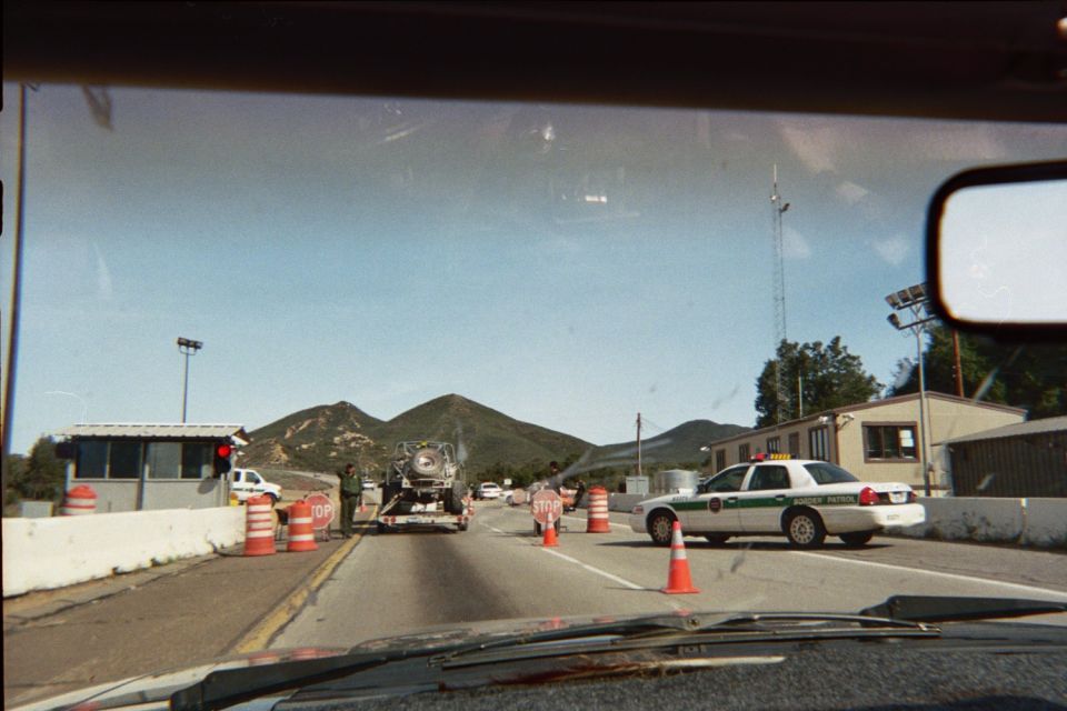 Windshield view of a checkpoint with a green-and-white patrol car and stop signs
