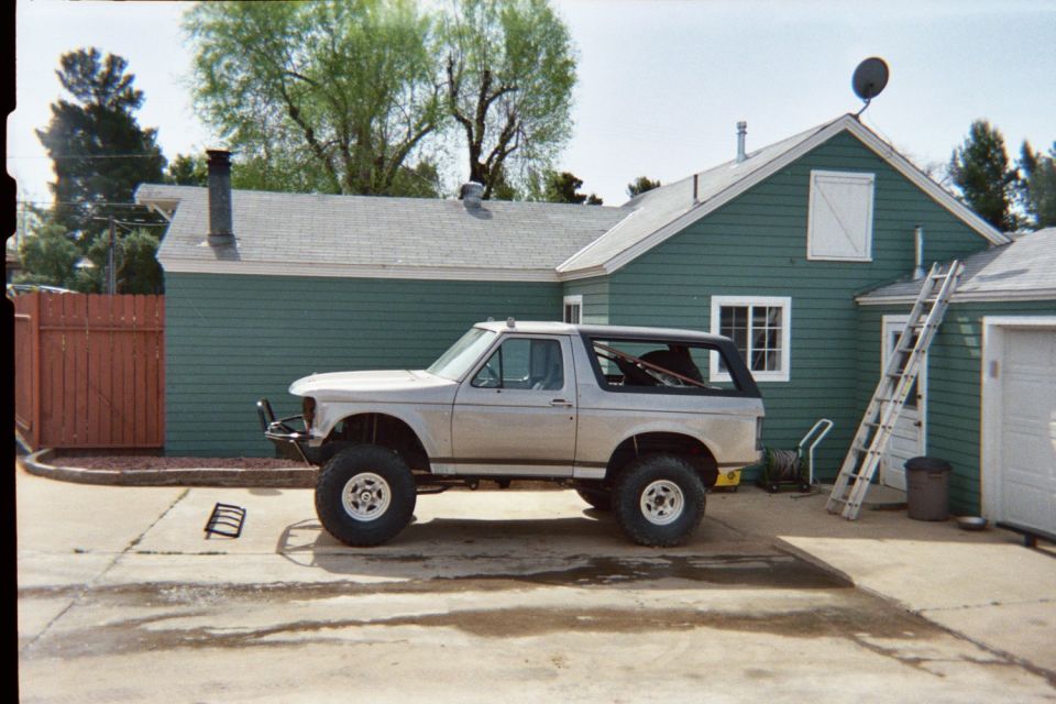 Lifted silver Ford Bronco SUV parked in a driveway beside a green house