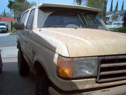 1988 Ford Bronco - A dusty 1987 Ford Bronco with a damaged windshield sits parked, showing its front three-quarter view.