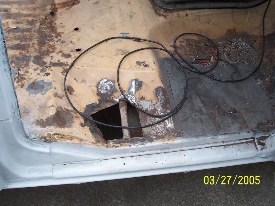 Interior floor of a vehicle with rust and a hole, wires are present