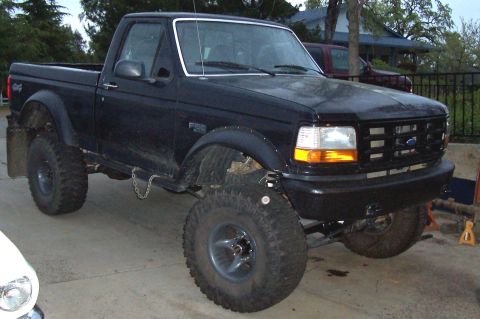 1986 Ford Bronco - This black Ford F-150 pickup truck features a lifted suspension and oversized tires, indicating off-road modifications.