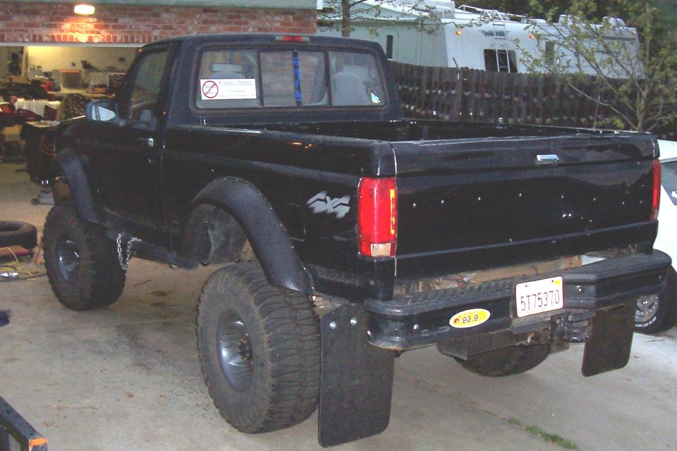Black pickup truck with large tires and mud flaps, rear view