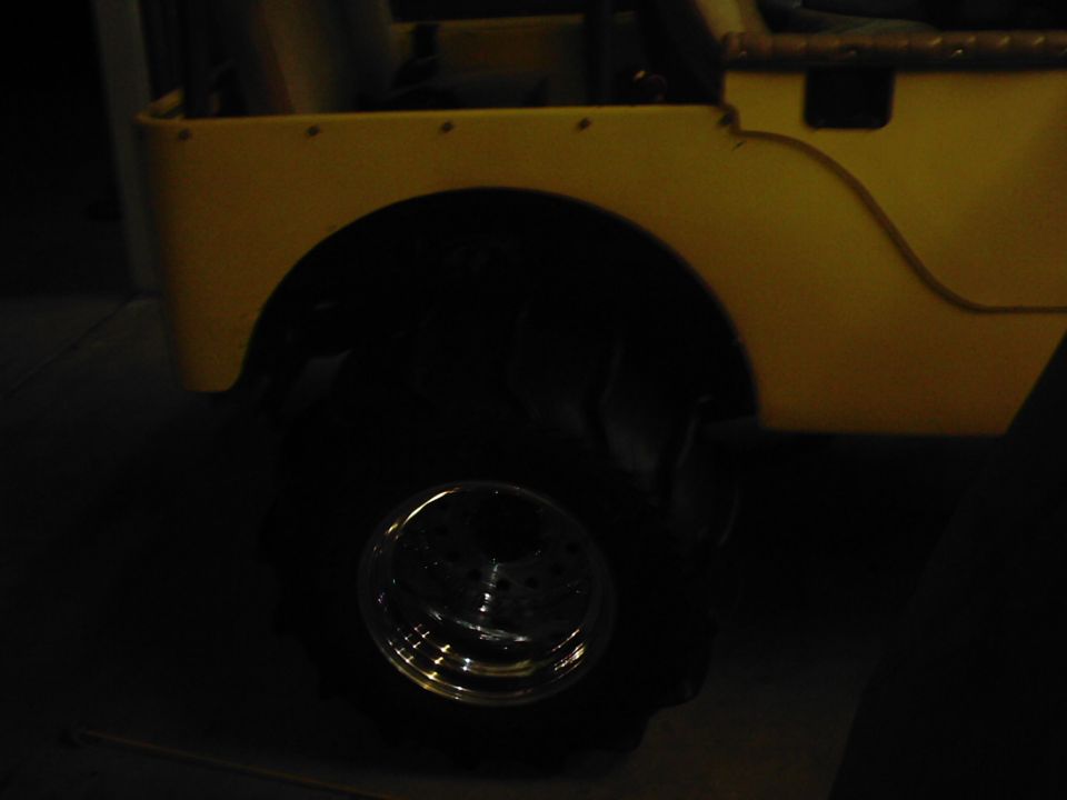 Side view of a yellow jeep with large tires and a chrome wheel. The body has a textured finish