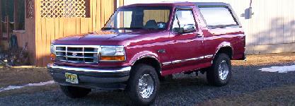 1971 Ford Mustang - A maroon Ford Bronco is parked on a gravel driveway in front of a wooden structure.