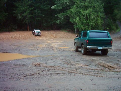 1978 Ford Bronco - Two SUVs navigate a muddy off-road course surrounded by trees.