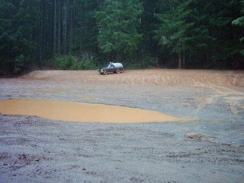 1978 Ford Bronco - A dark-colored SUV navigates a wet, muddy area with trees in the background.