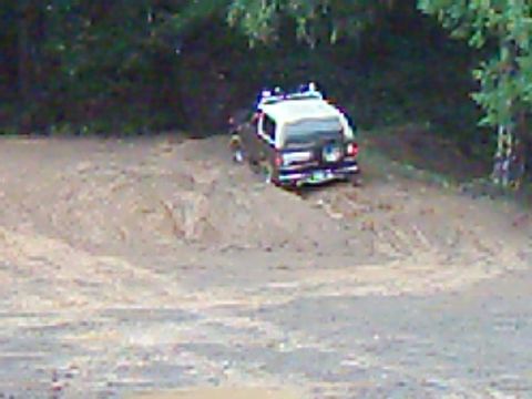 1978 Ford Bronco - An SUV navigates a muddy, uphill terrain surrounded by dense foliage.