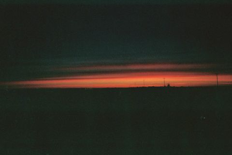 1990 Ford Bronco - moody sunset with a band of orange light along a dark flat horizon, with faint distant structures silhouetted against the sky.