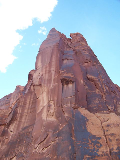 1991 Ford Bronco - A towering red rock formation dominates the frame under a bright blue sky with scattered clouds.